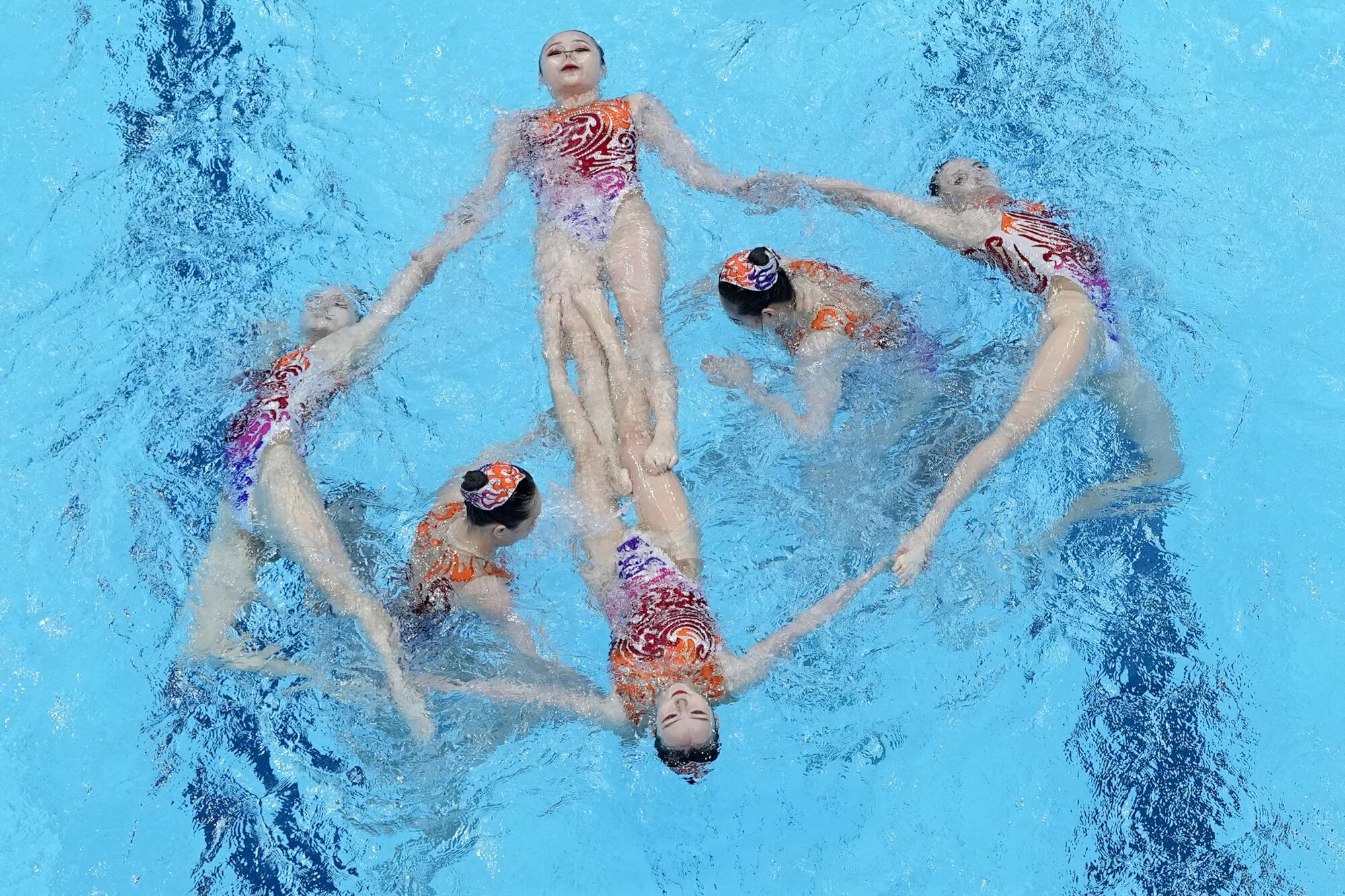 Members of the China artistic swimming team hold hands or legs on the water surface to create a design while two float in it