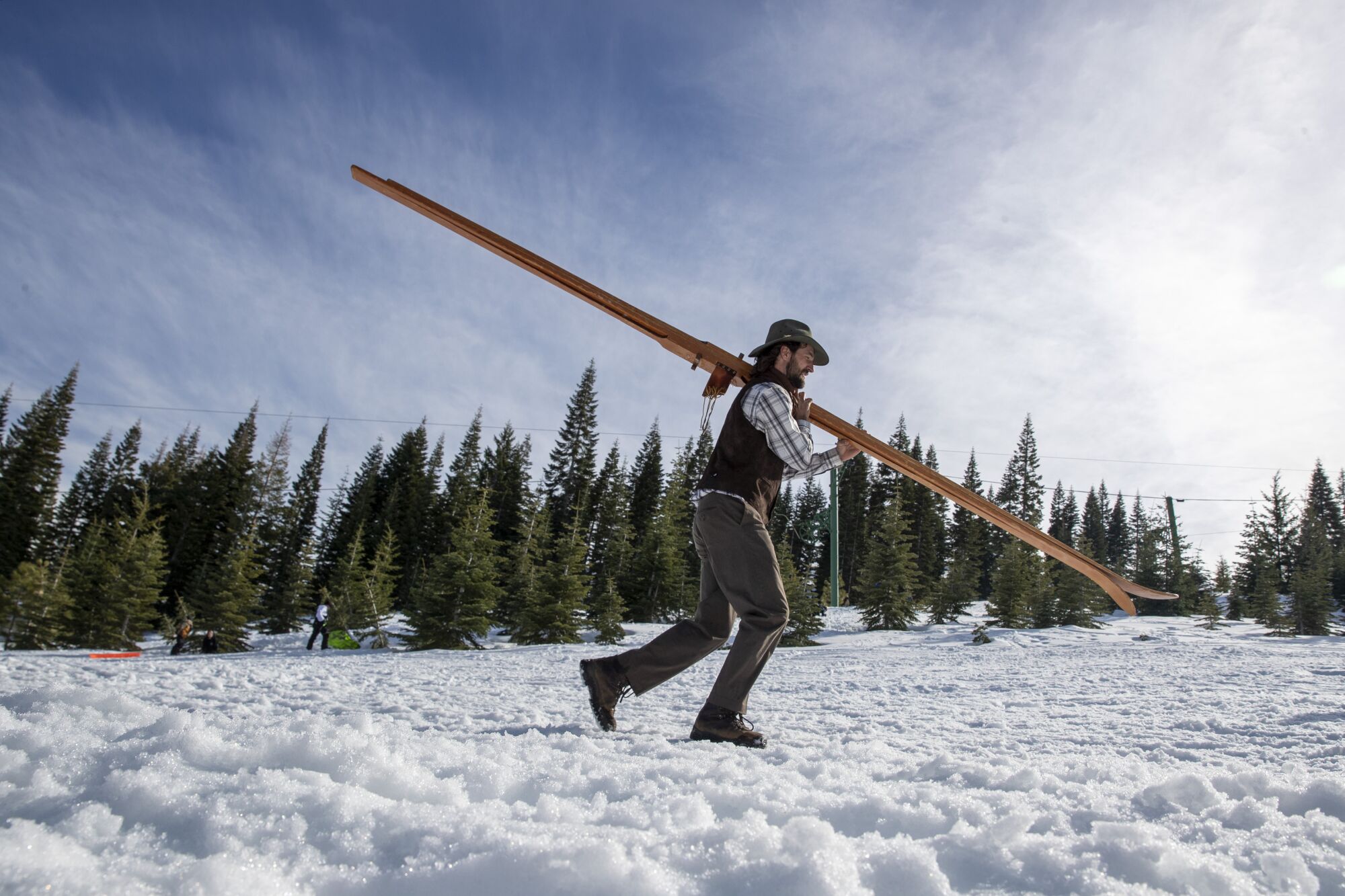 A longboard racer carries his skis through the snow