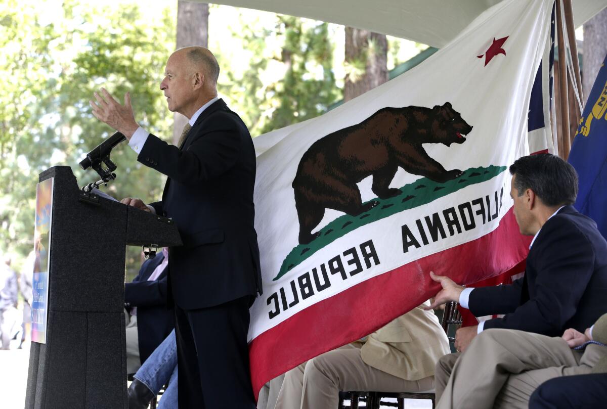 Nevada Gov. Brian Sandoval, right, helps out California Gov. Jerry Brown, left, by pulling in the California flag that was wrapping around Brown as he spoke at the 18th Annual Lake Tahoe Summit on Tuesday.