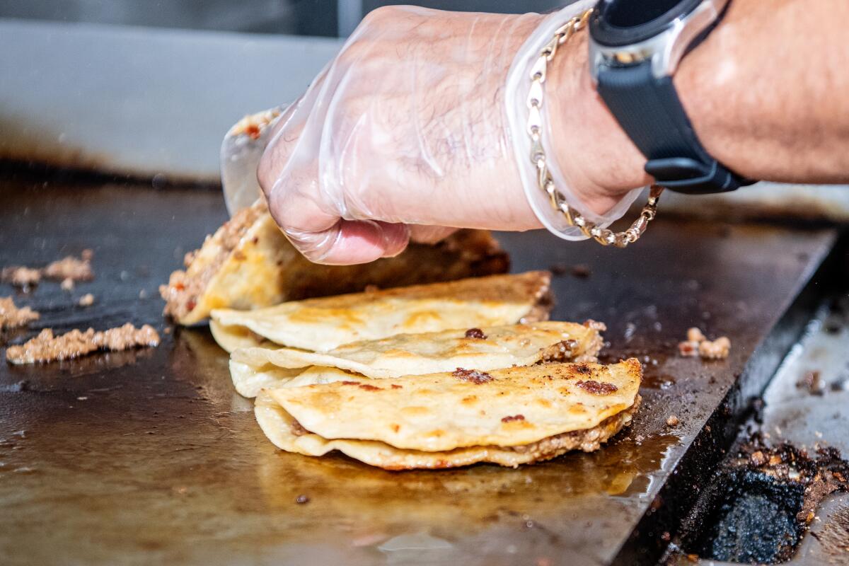 A hand flips tacos on a flat-top grill
