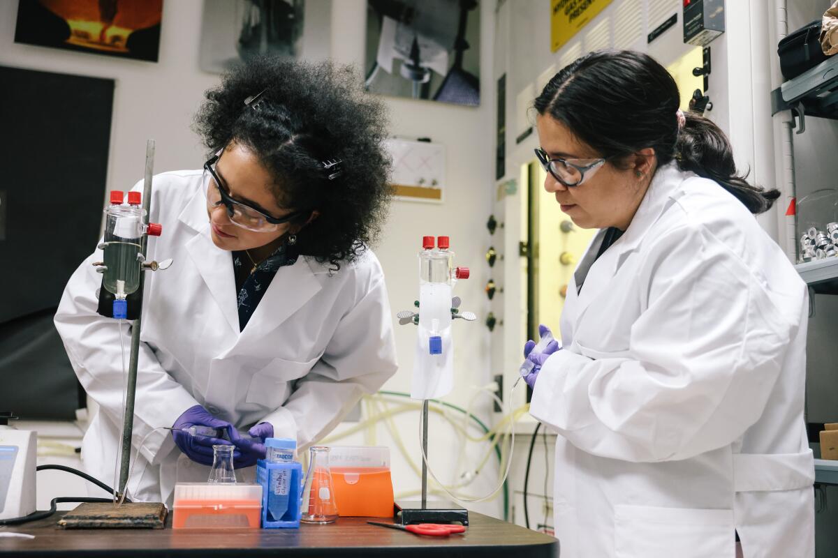 Women in lab coats observe an experiment in a JPL lab (well / Los Angeles Times)