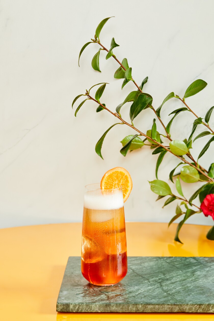 A glass full of liquid with a slice of orange on the side.