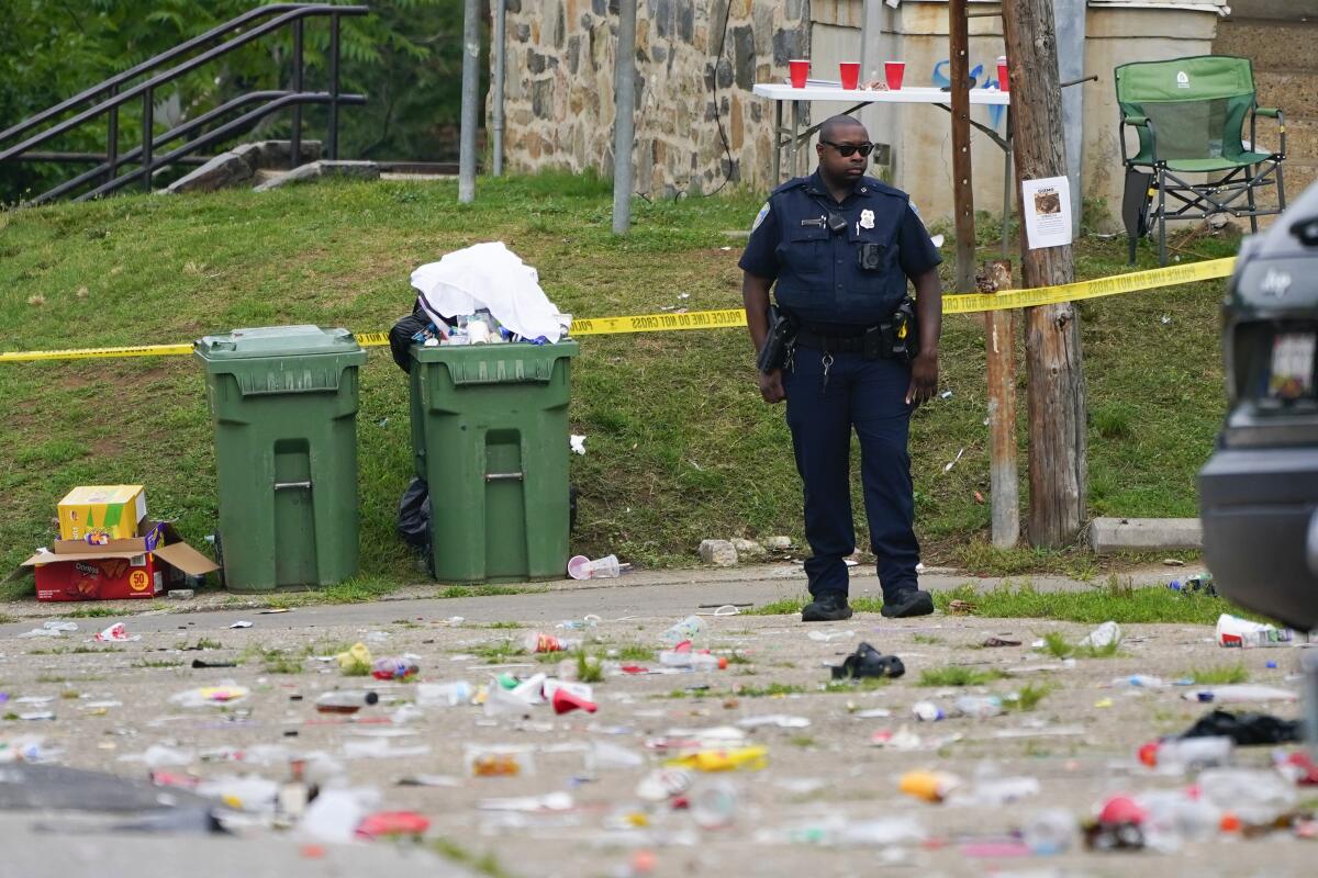 A police officer standing near police tape and trash cans in an area strewn with debris.
