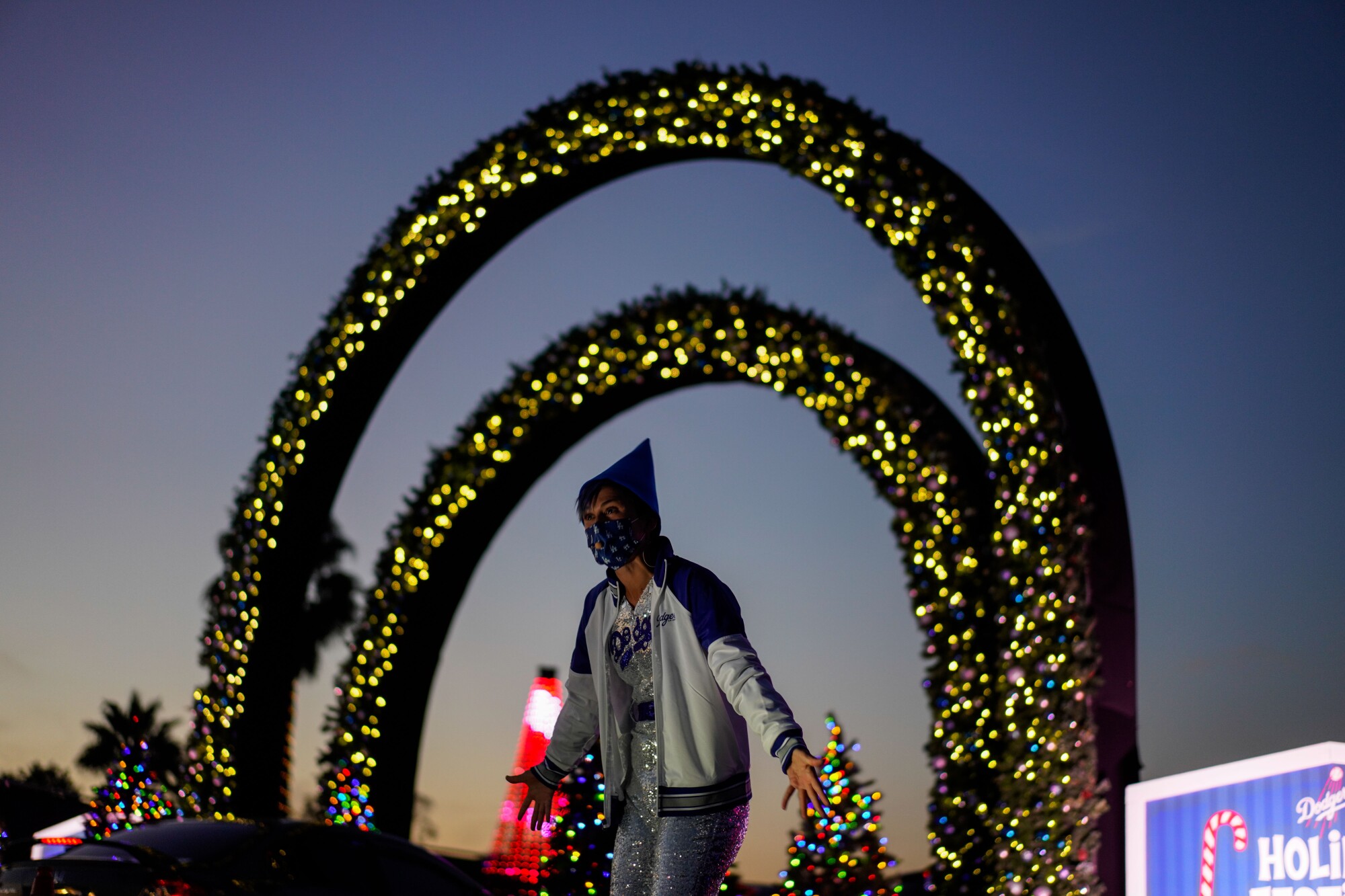 A performer decked out in a Christmas themed waves at cars making their way through the Dodger's Holiday Festival