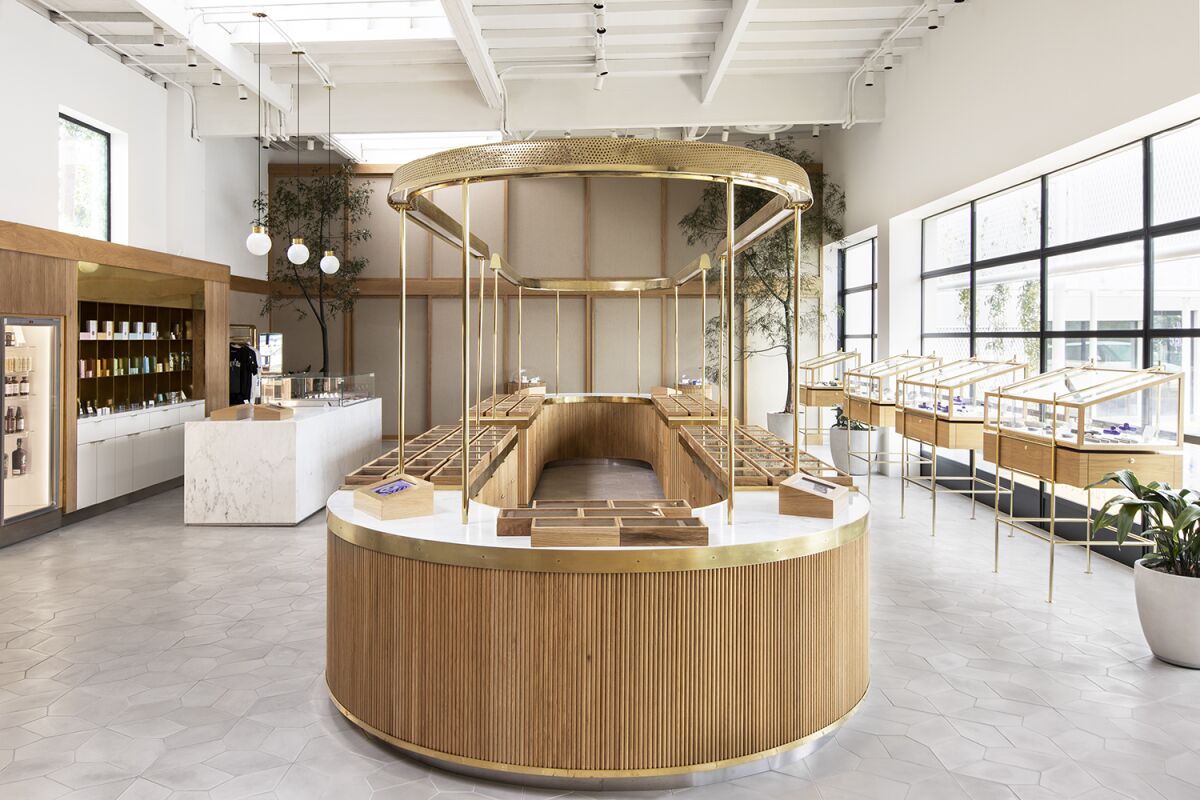 An oval-shaped, wood- and brass-fronted counter in the middle of a brightly lit dispensary