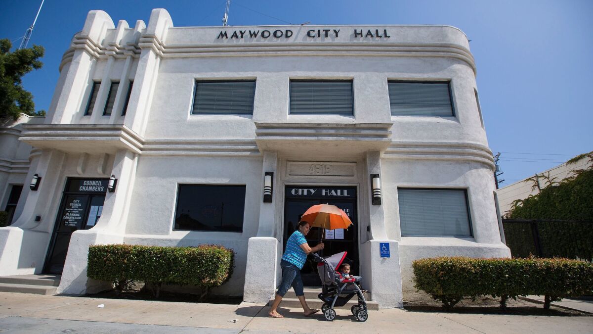 A woman pushes a toddler in a stroller past Maywood City Hall in 2016.