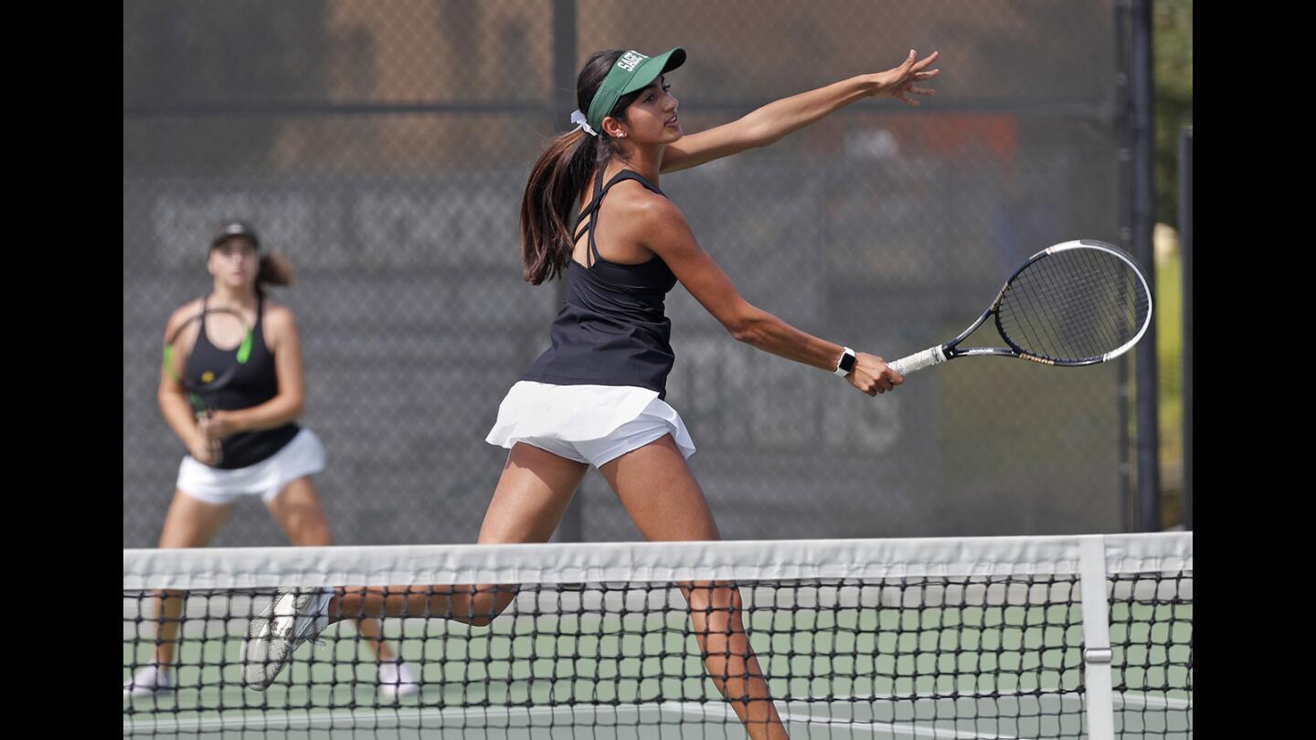 Sage Hill School's Karina Grover, center, scores at the net as partner Miranda deBruyne, left, looks on during a No. 1 doubles set against Mater Dei in a nonleague tennis match in Newport Beach on Tuesday, August 28.
