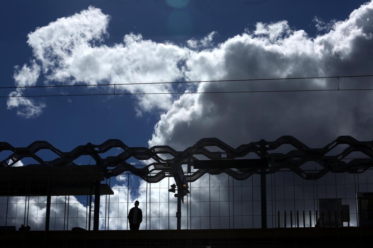 A person standing at a light rail station silhouetted by passing clouds