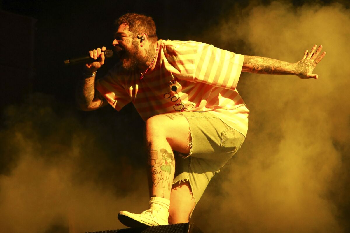 A man wearing cutoff shorts and a shirt holds a microphone while dancing on a stage