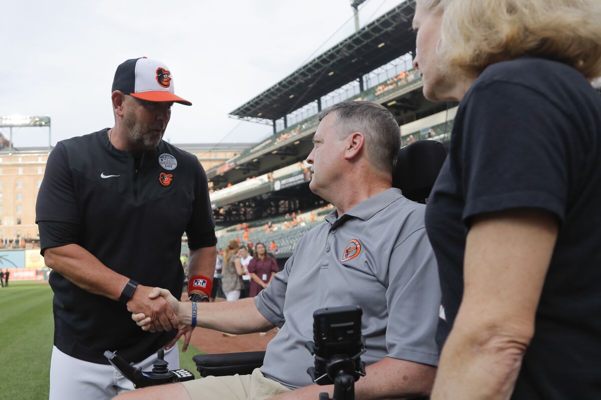 Baltimore Orioles manager Brandon Hyde, left, talks with former Orioles pitcher Jim Poole, center, and his wife, Kim Poole, prior to a baseball game against the Seattle Mariners, Thursday, June 2, 2022, in Baltimore. The Orioles honored Lou Gehrig Day on Thursday. (AP Photo/Julio Cortez)
