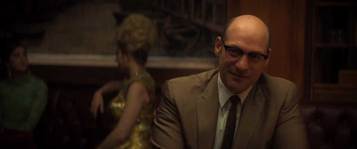 Junior Soprano, played by a bespectacled Corey Stoll, sits at a table in “The Many Saints of Newark.”
