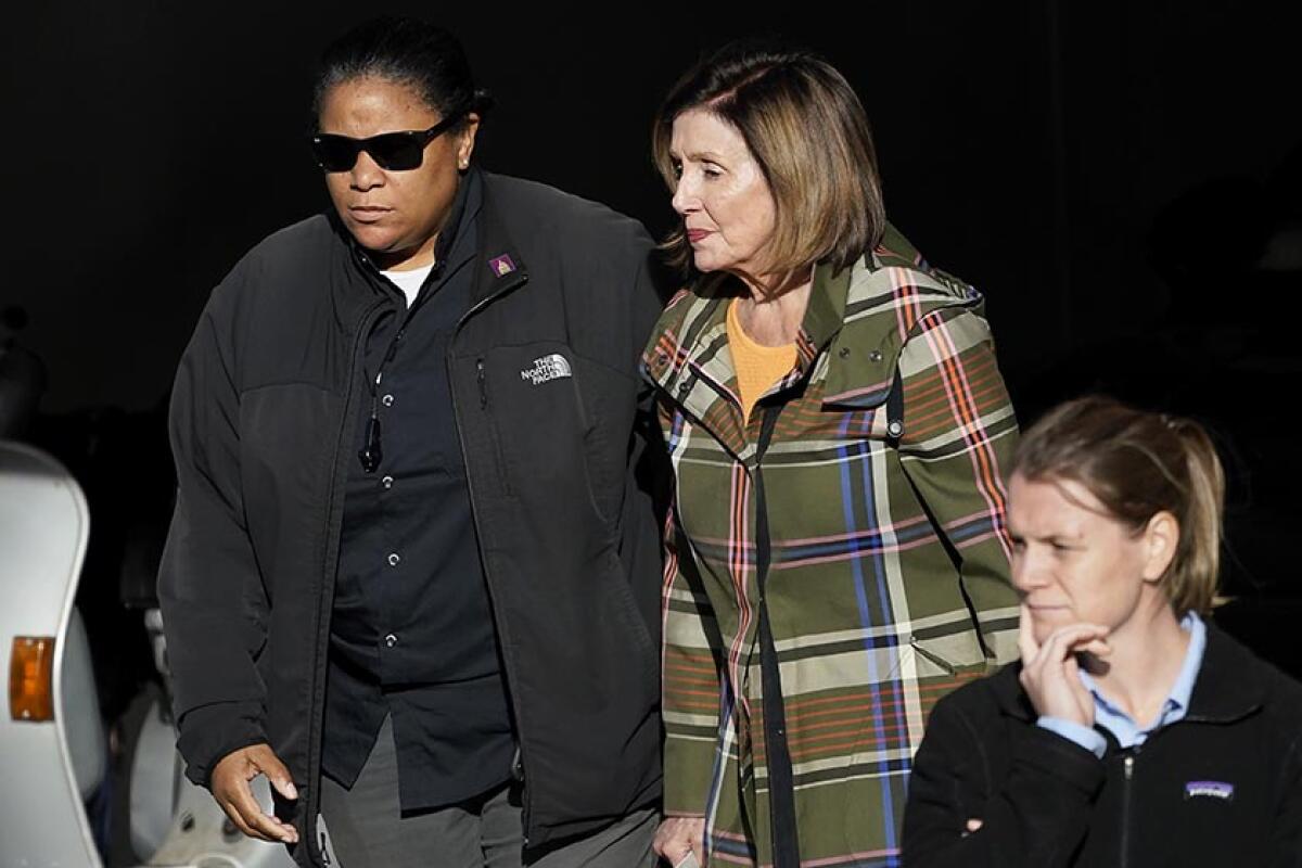 A woman in a dark jacket escorts an older white woman in a plaid coat.