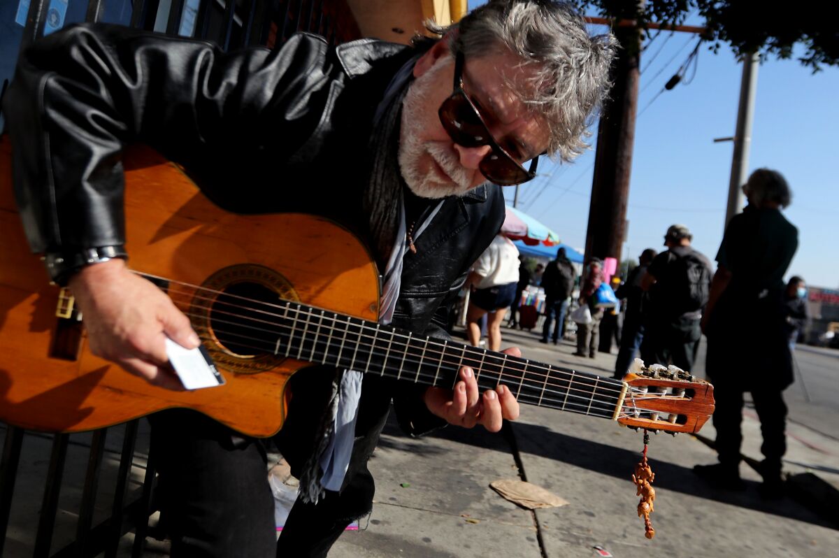 Jesse Aleman, a self-styled troubador, plays guitar for people waiting for a meal