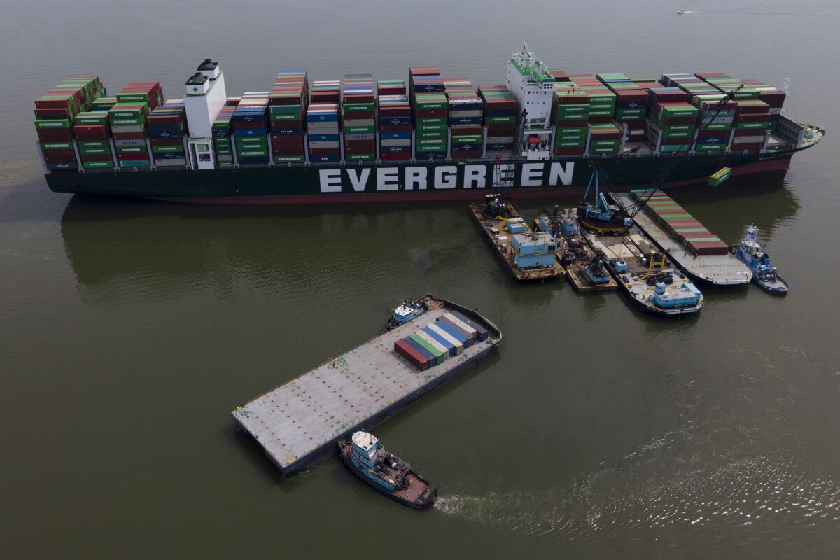 FILE - Tugboats, bottom, align a barge near the container ship Ever Forward, top, which ran aground in March 2022 as workers remove containers from it in efforts to lighten the load and refloat the vessel, April 13, 2022, in Pasadena, Md. The ship has been stuck in the channel since March 13. A Coast Guard investigation into the grounding in March of a cargo ship in the Chesapeake Bay is faulting the pilot tasked with helping the ship navigate the waterway. (AP Photo/Julio Cortez, File)