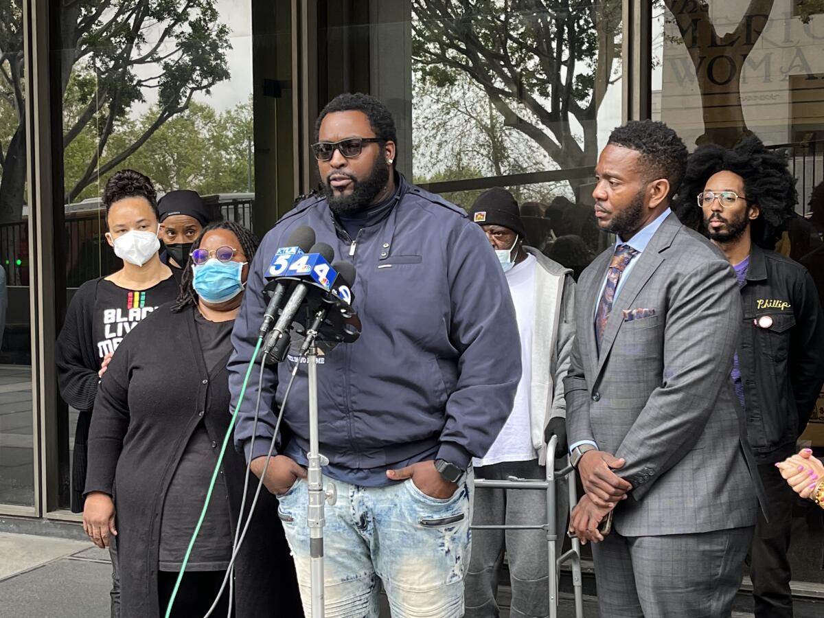 A man in sunglasses speaks into a microphone to a crowd outside a court building