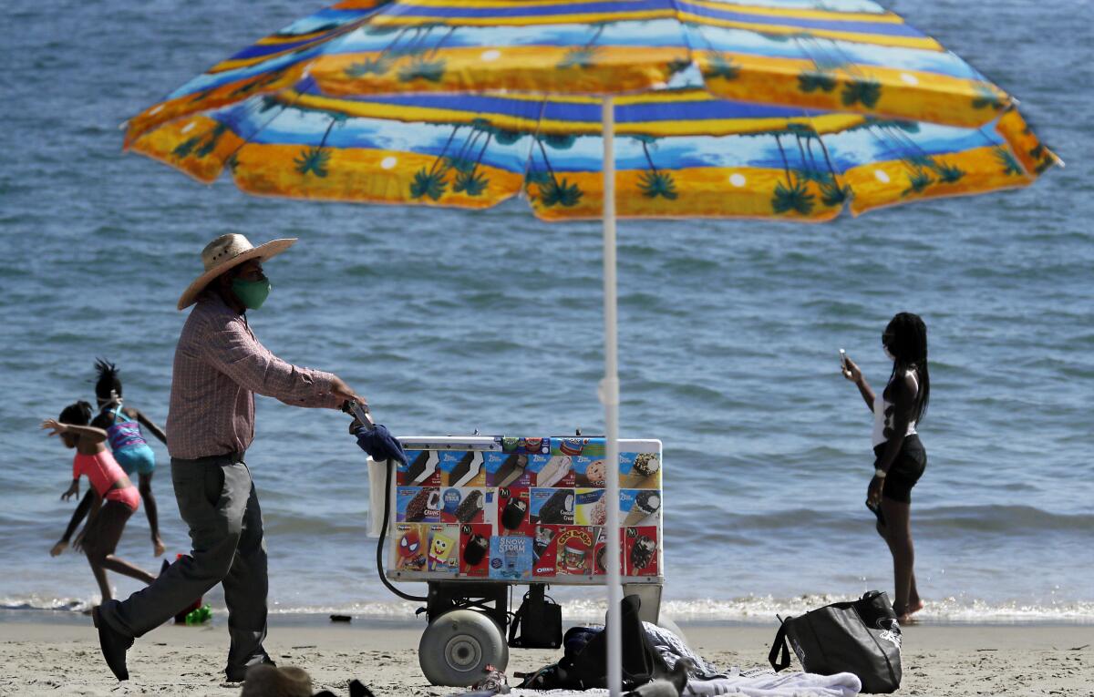 An ice cream vendors pushes a cart along the sand at Junipero Beach in Long Beach on a warm afternoon.