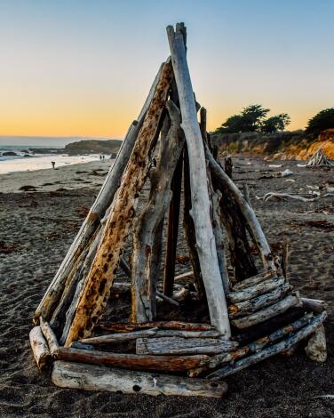 A small pyramidal structure made from driftwood on a beach