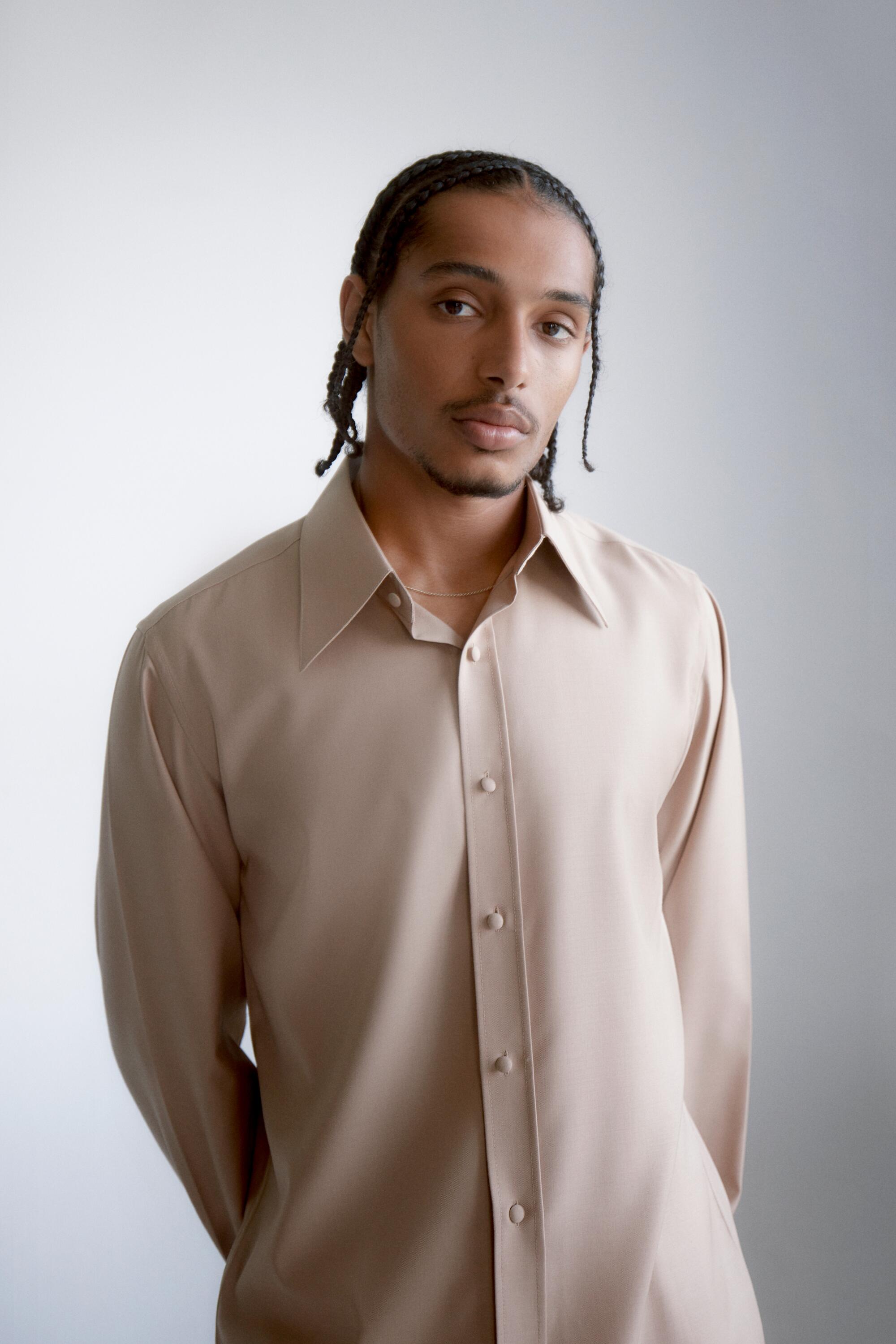 A male model wearing a beige collared shirt looks directly at the camera.