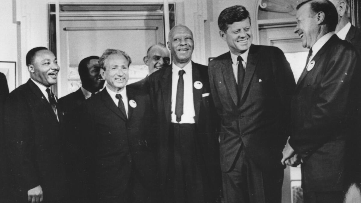 A black-and-white photo of Martin Luther King Jr., left, Rabbi Joachim Prinz, A. Philip Randolph and President Kennedy, among other men in suits.