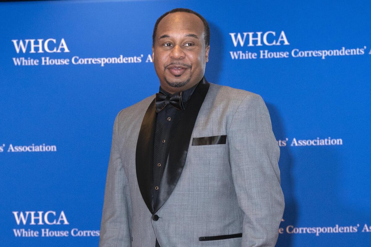 Roy Wood Jr. in a gray suit with a black  shirt and tie.