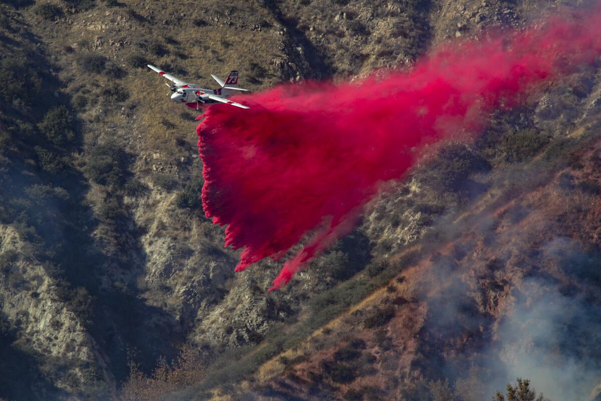 An airplane drops bright pink fire retardant on a forest.