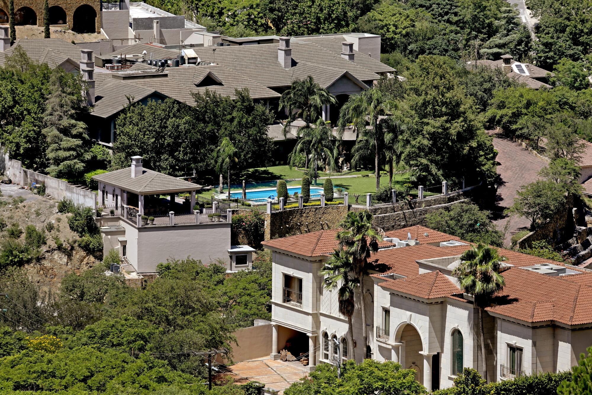 An overhead view of homes with swimming pools and green lawn and trees. 