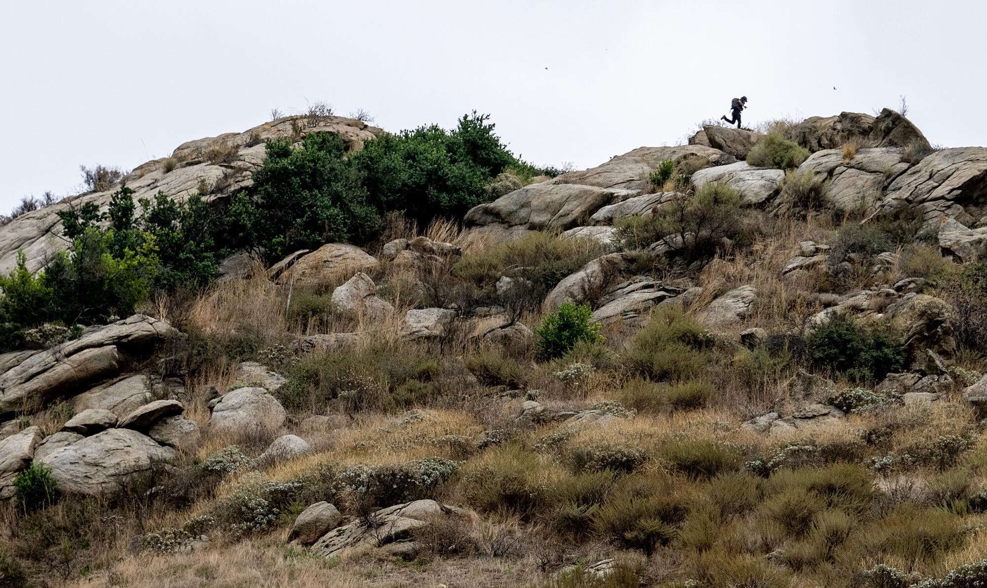 A lone figure runs atop a large rocky hill.