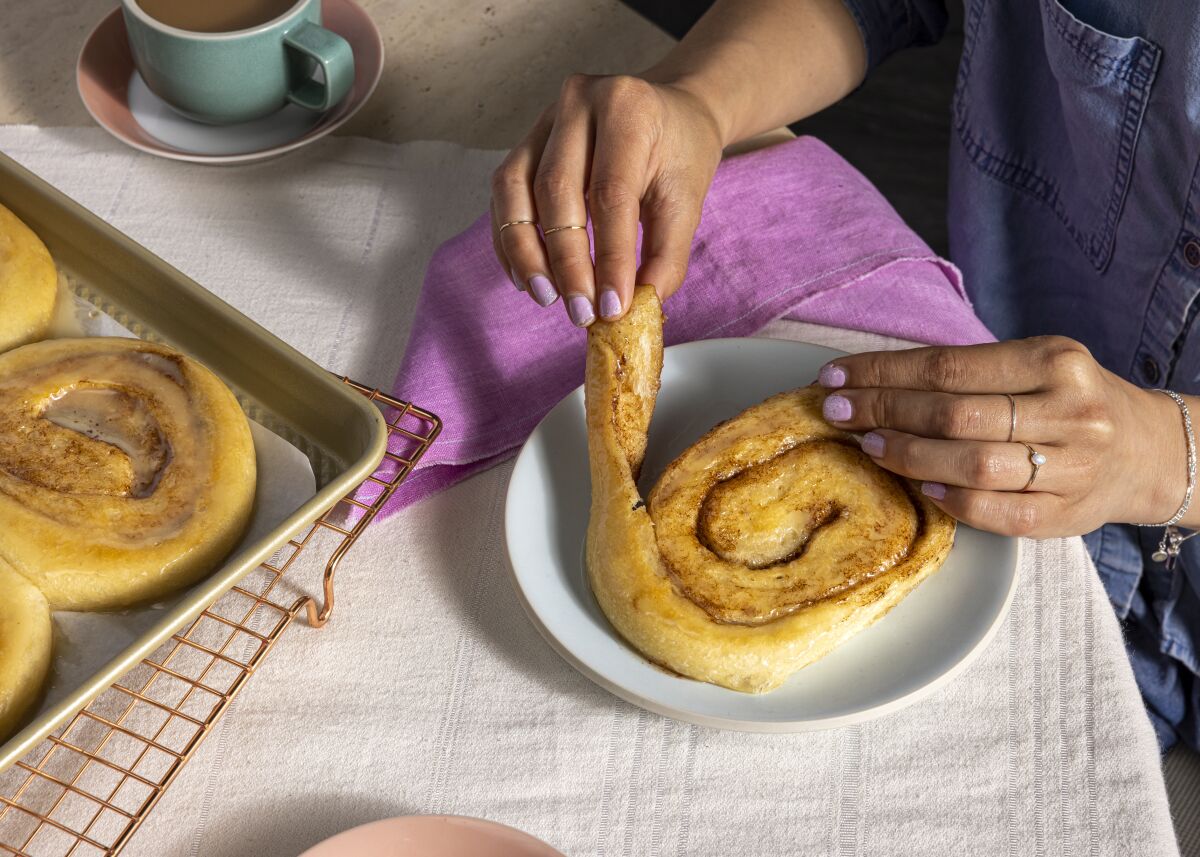 Closeup of a person's hands unrolling a honey bun on a plate.