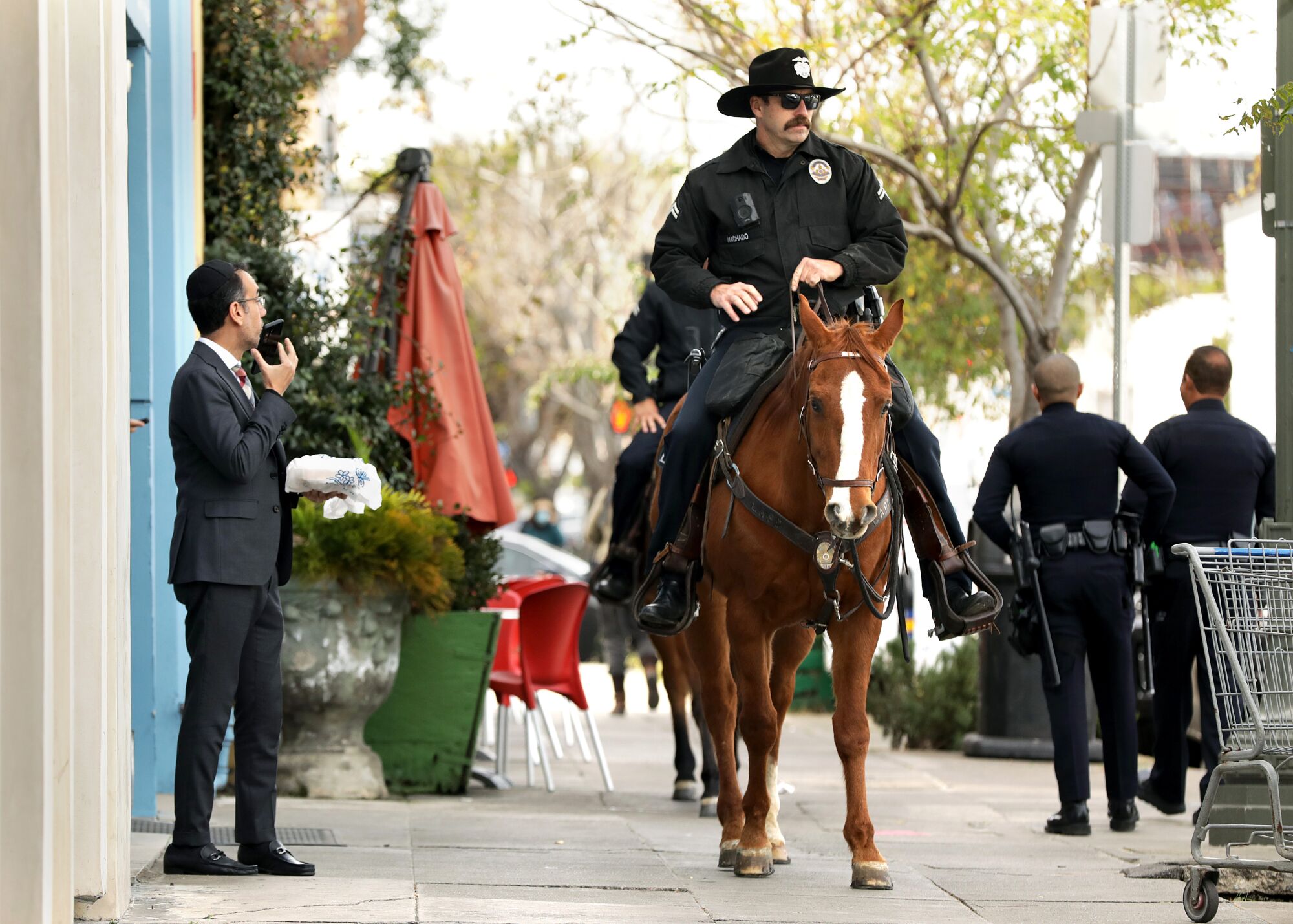 LAPD officers on horseback patrol along Pico Boulevard while a passerby looks on.