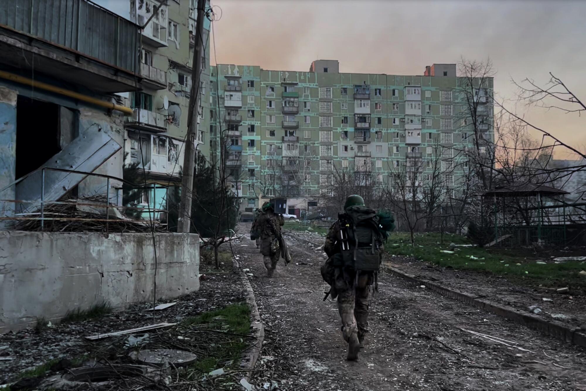 Soldiers file past bomb-shattered apartment buildings.