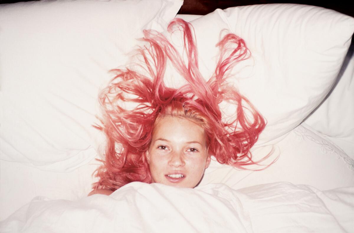 An overhead portrait of Kate Moss shows the model with pink hair on a bed.