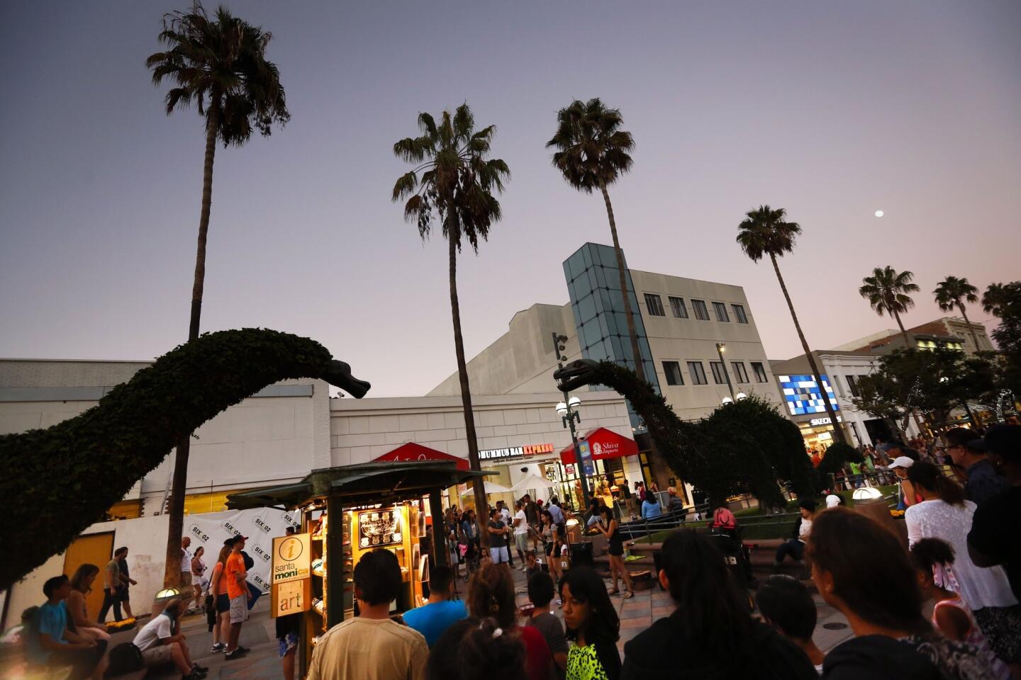 Twin sisters Celina and Carolyn Nguyen, 24, of Santa Ana, perform underneath the dinosaur topiaries on the Third Street Promenade on Saturday, Sept. 6, 2014.