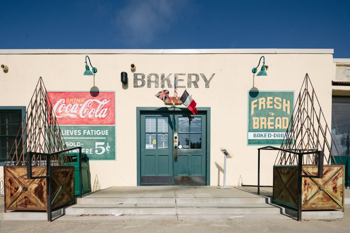 A one-story building with "bakery" painted over the door and other vintage-looking signs on either side of the door