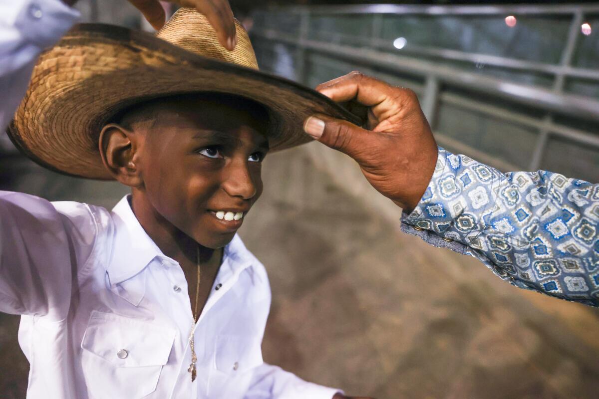 A boy smiles as another person's hand touches his cowboy hat.