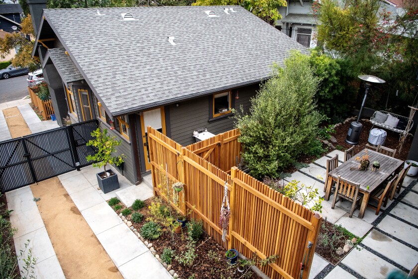 The front house and a patio with a wooden dining table are seen from above 