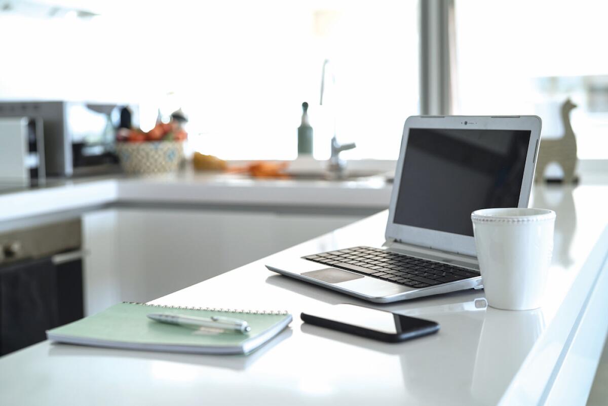 A laptop computer, smartphone and notebook are among items on a kitchen counter