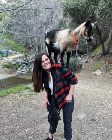 A woman with a goat on her back on a hike.  
