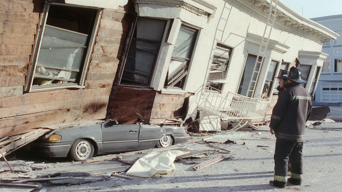 In one of the hardest-hit areas in the 1989 Loma Prieta earthquake, two firemen look at a collapsed building that crushed a car in San Francisco's Marina District.