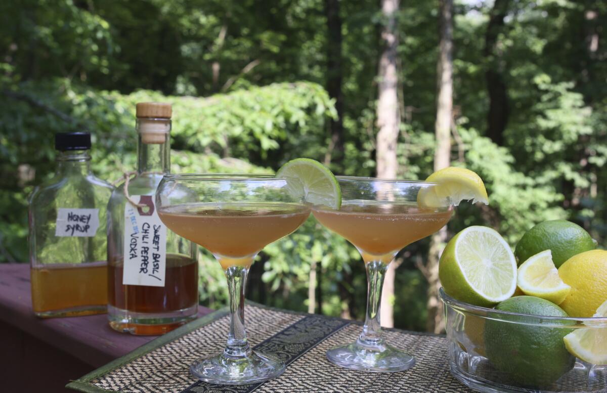 Cocktails containing alcohol and syrup infusions sit amid bottles and mixing accessories in Allison Park, Pa., on July 4, 2021. Alcohol and syrup infusions are growing in popularity and are relatively simple to incorporate into home bars. (AP Photo/Ted Anthony)