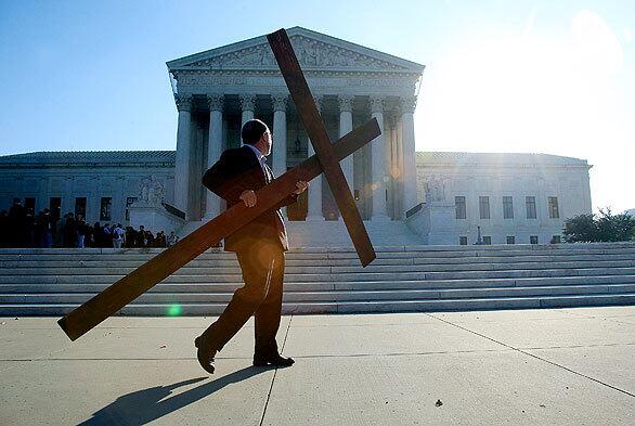 The Rev. Patrick Mahoney of the Christian Defense Coalition carries a cross in front of the U.S. Supreme Court building. Today, the high court will hear oral arguments in a case involving a memorial with a cross, erected by the Veterans of Foreign Wars in a remote area within what is now a federal preserve.
