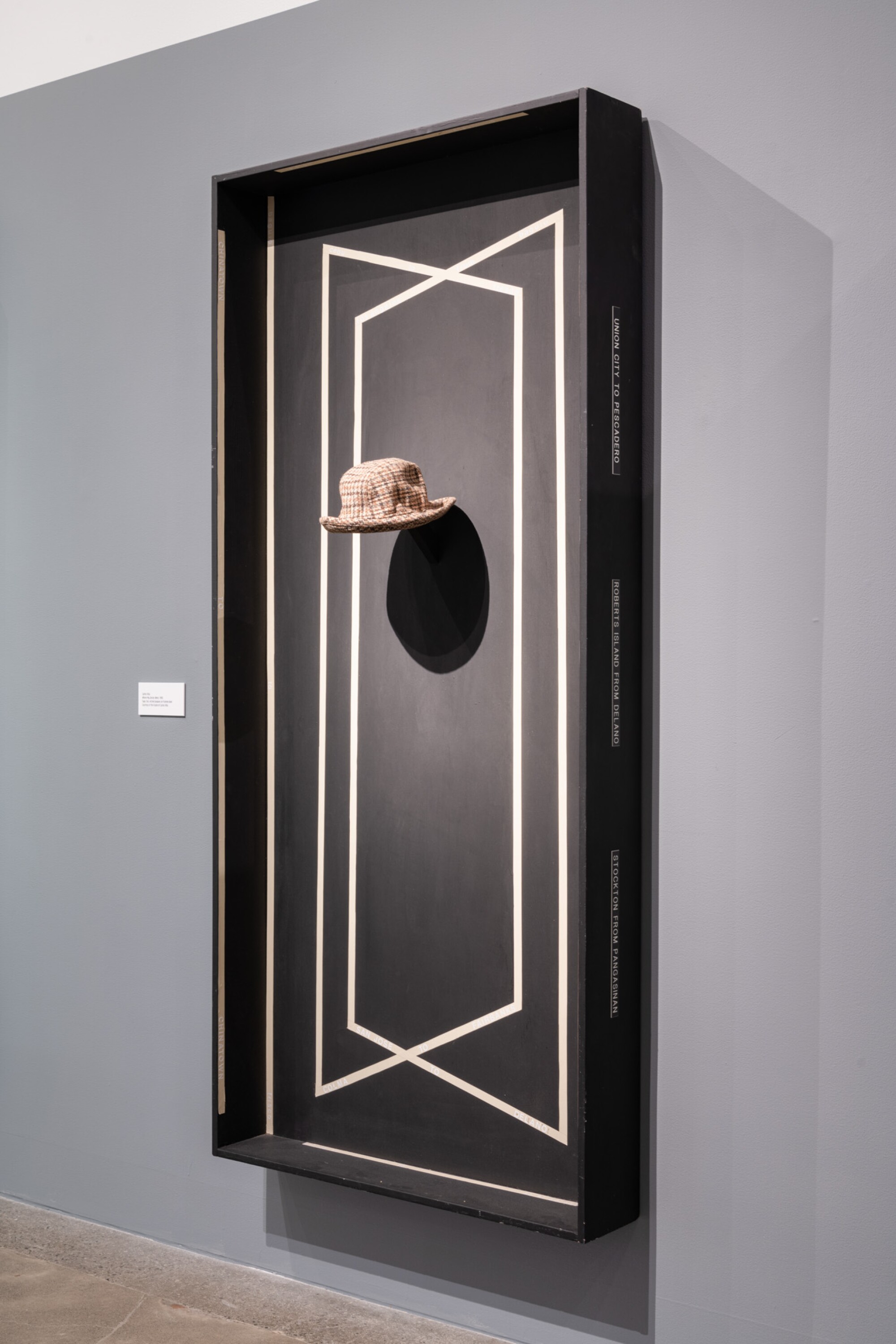 A wall sculpture by Carlos Villa shows a man's fedora suspended before a black panel that resembles a doorway.