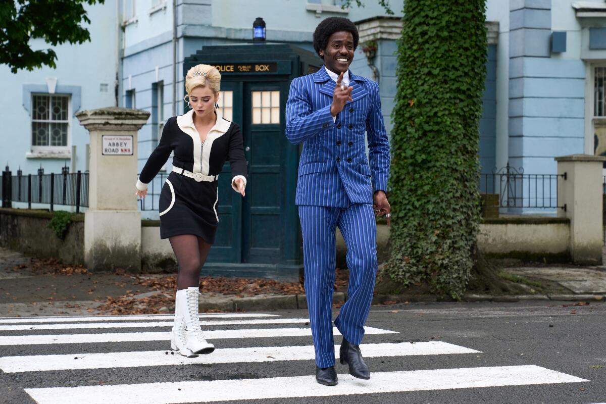 Ruby Sunday and the Doctor walk in a crosswalk with the TARDIS behind them.