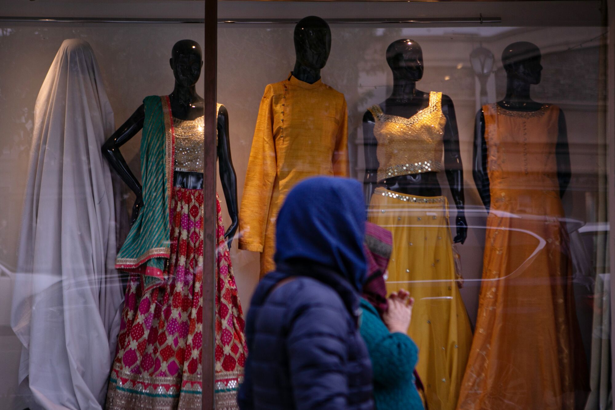 Women walk by a storefront display of garments 