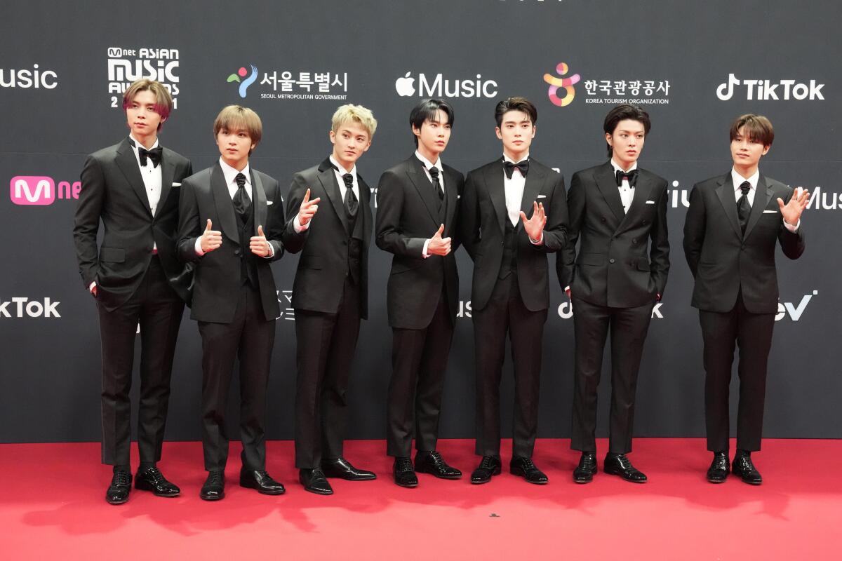 Seven members of the K-pop group NCT 127 posing in tuxedos on a red carpet