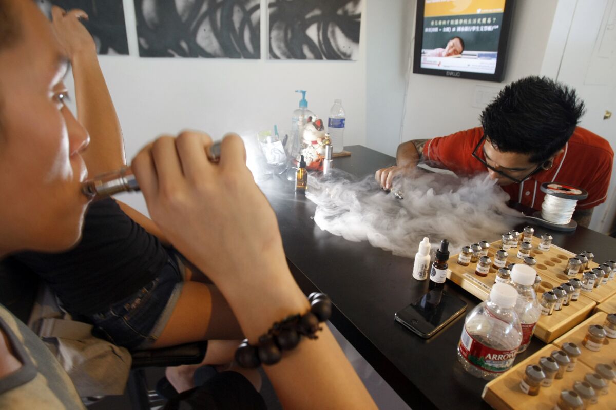 Brian Jung, left, draws in on an electronic cigarette as Aaron Flores exhales water vapor at Aqua Vape in Temple City in 2013.