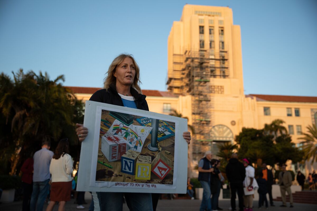 Mama Becker-Varano holds protest sign Tuesday at Waterfront Park at vigil for victims of Tuesday's shooting in Uvalde, Texas.