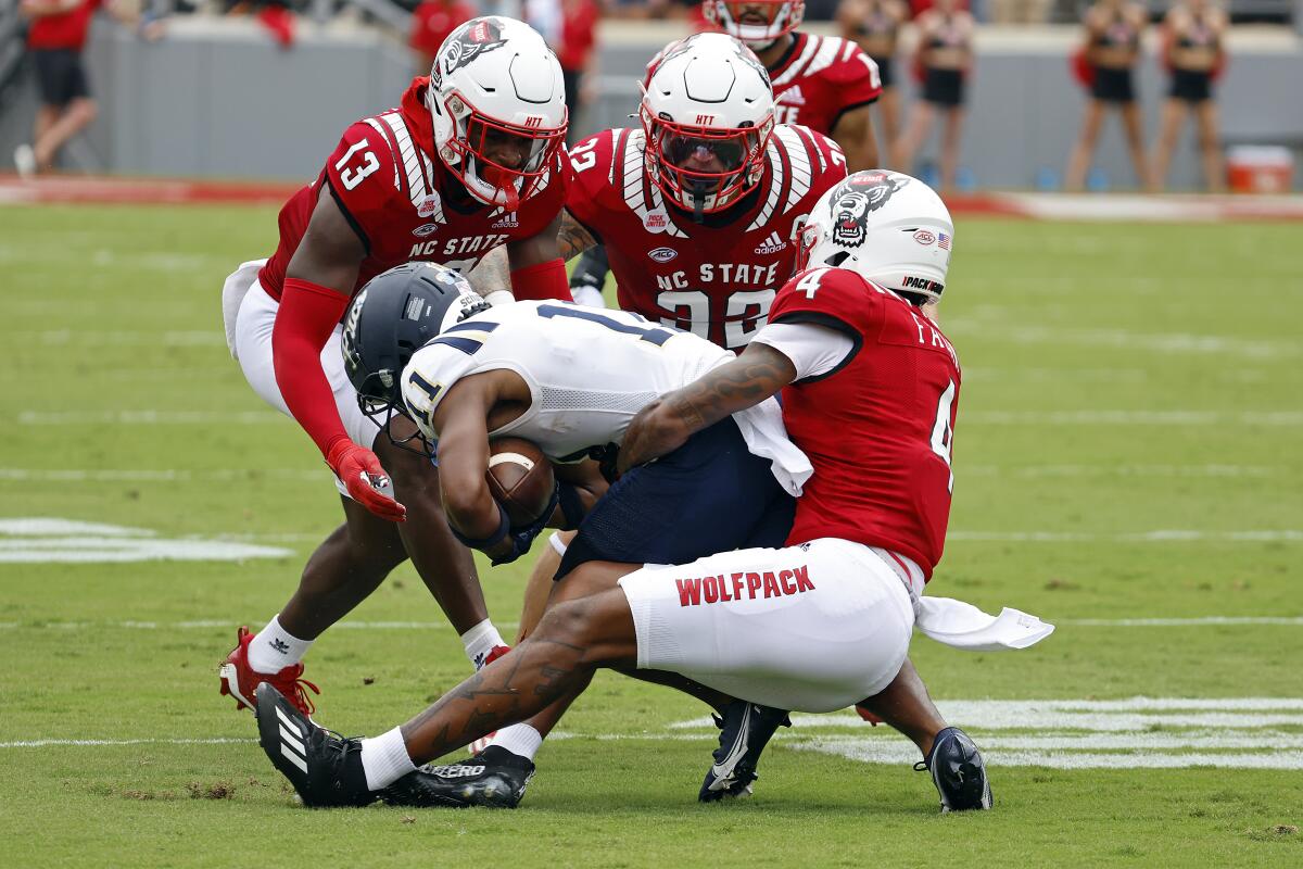 Charleston Southern's Vinson Davis (11) is tied up by North Carolina State's Cyrus Fagan (4), Drake Thomas (32) and Tyler Baker-Williams (13) during the first half of an NCAA college football game in Raleigh, N.C., Saturday, Sept. 10, 2022. (AP Photo/Karl B DeBlaker)