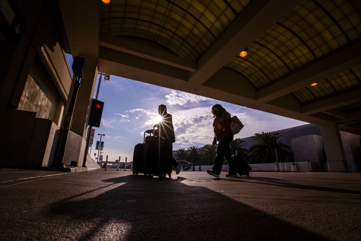 Travelers walk with their luggage at John Wayne Airport.