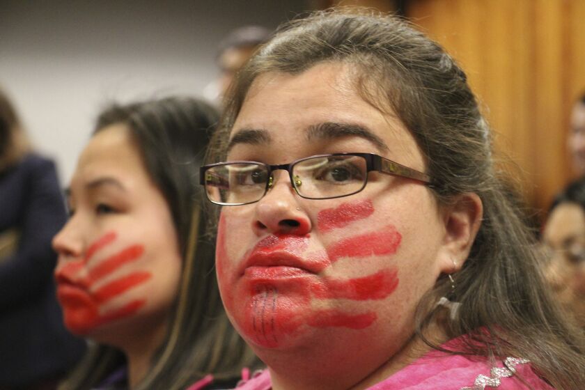 Joanne Sakar, left, and Natasha Gamache hold a silent protest in a courtroom, to highlight what Gamache says is Alaska's history of not properly investigating, prosecuting or sentencing perpetrators of crimes against Alaska Native women, in Anchorage, Alaska, Monday, Oct. 21, 2019. They attended the arraignment for Brian Steven Smith, who faces 14 charges in the deaths of two Alaska Native women. The red hands painted on their faces represents the silencing of indigenous women. (AP Photo/Mark Thiessen)