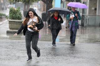 SANTA MONICA, CA - DECEMBER 20, 2023 - People make their way across Broadway during a morning downpour in Santa Monica on December 20, 2023. The first of two storm systems is bringing rain to parts of the Southland today, providing a preview of the second, more powerful system that forecasters say will give the region a more thorough dose of precipitation.(Genaro Molina/Los Angeles Times)